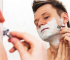Man shaves face with a safety razor and shaving cream in mirror.
